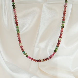 Natural multi-color Tourmaline oval bead necklace on white satin fabric, pink and green beads with yellow gold and diamond spacers.