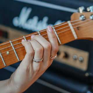 Hand with diamond band and gold wedding band playing e minor on electric guitar.