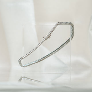 White gold tennis bracelet with round brilliant natural Diamonds curving over a clear block, box clasp in frame.
