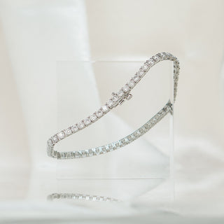 Round brilliant natural Diamond tennis bracelet in white gold, strand angled across a clear acrylic block.