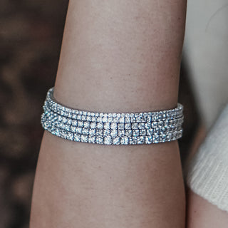 Stacked white gold Diamond tennis bracelets worn on the arm, multiple widths layered against a dark background.