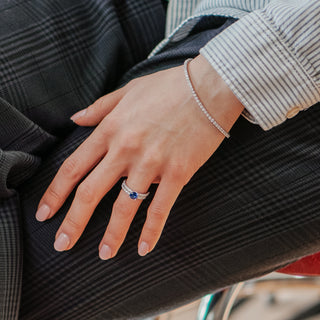 Lab grown diamond tennis bracelet in white gold worn on the wrist, hand resting on dark pleated fabric.