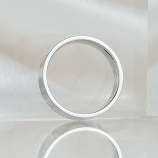 Flat profile white gold wedding band standing upright, showing the 5.1mm width and squared edges against a soft neutral backdrop.