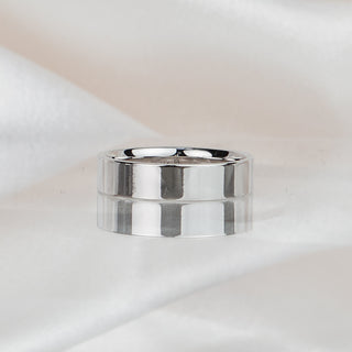 Wide flat wedding band in 14k white gold resting on draped ivory fabric, brushed light catching the flat outer surface.