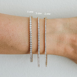 Three widths of lab diamond tennis bracelets worn on the wrist, 2, 3, and 5 ctw sizes side by side in yellow gold