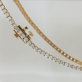 Yellow gold tennis bracelet with round brilliant lab diamonds, prong set stones curving along the strand with clasp in frame.