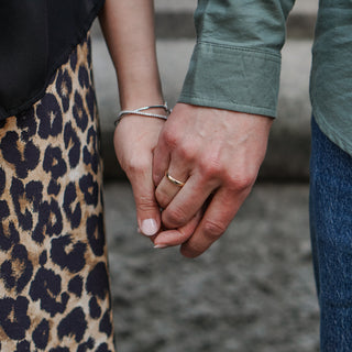 Couple holding hands outdoors, one wearing a yellow gold half-round wedding band, candid worn view.