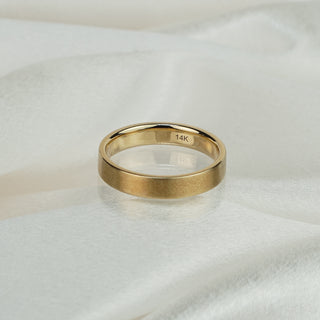 14k yellow gold flat wedding band with comfort fit interior on white satin fabric, 14K hallmark visible inside.