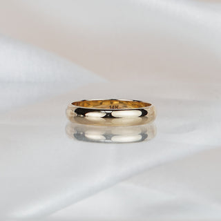 Polished yellow gold half-round wedding band on draped ivory fabric, high shine across the domed surface.