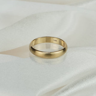 14k yellow gold half-round wedding band with satin finish resting on white satin fabric, 14K hallmark visible inside the band.