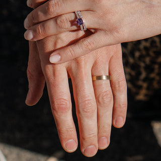 Couple holding hands, one wearing a flat yellow gold wedding band, worn view showing the band's low profile on the finger.